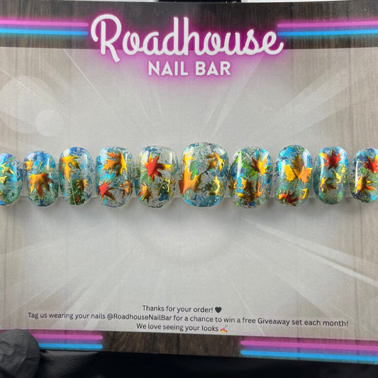 Hand-painted press-on nails with glass-effect base, aqua foiling, and metallic copper autumn leaves, displayed on Roadhouse Nail Bar backing card.