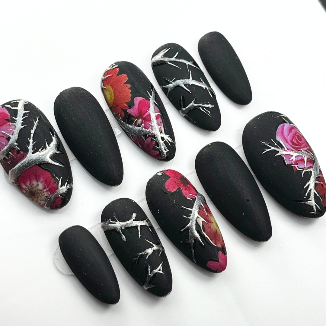 10-piece matte black press-on nail set with chrome thorn detailing and red floral accents, shown in medium almond shape for gothic summer style