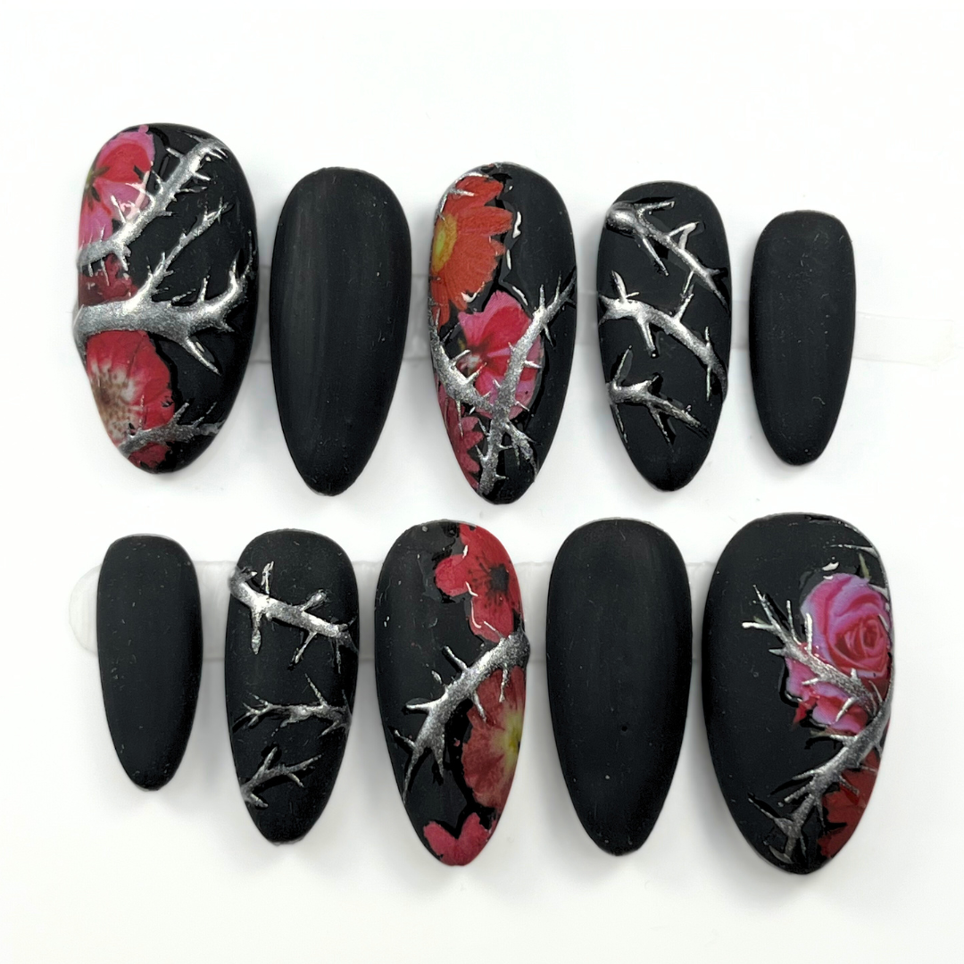 10-piece matte black press-on nail set with chrome thorn detailing and red floral accents, shown in medium almond shape for gothic summer style