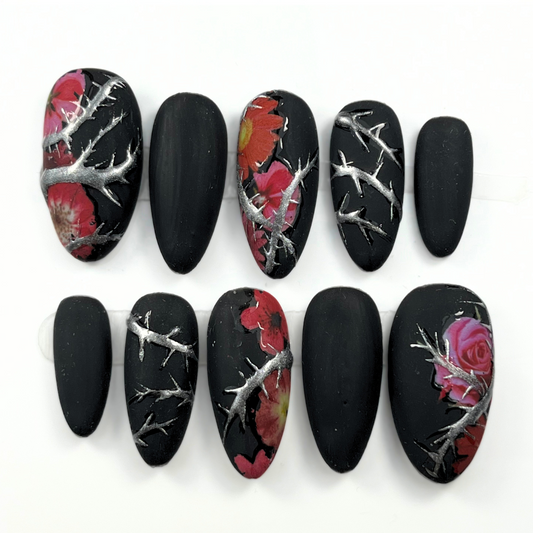 10-piece matte black press-on nail set with chrome thorn detailing and red floral accents, shown in medium almond shape for gothic summer style
