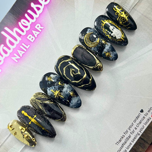 Black and gold gothic press-on nail set featuring celestial stars, moons, and baroque gold accents on a cosmic background.