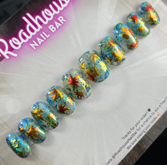 Hand-painted press-on nails with glass-effect base, aqua foiling, and metallic copper autumn leaves, displayed on Roadhouse Nail Bar backing card.