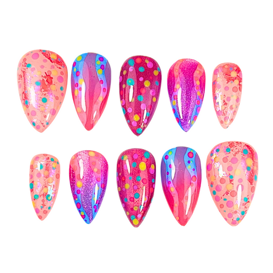 Hand-painted press-on nails in vibrant neon pinks, purples, and oranges with glitter, swirls, and multicoloured dot accents, festival-inspired.