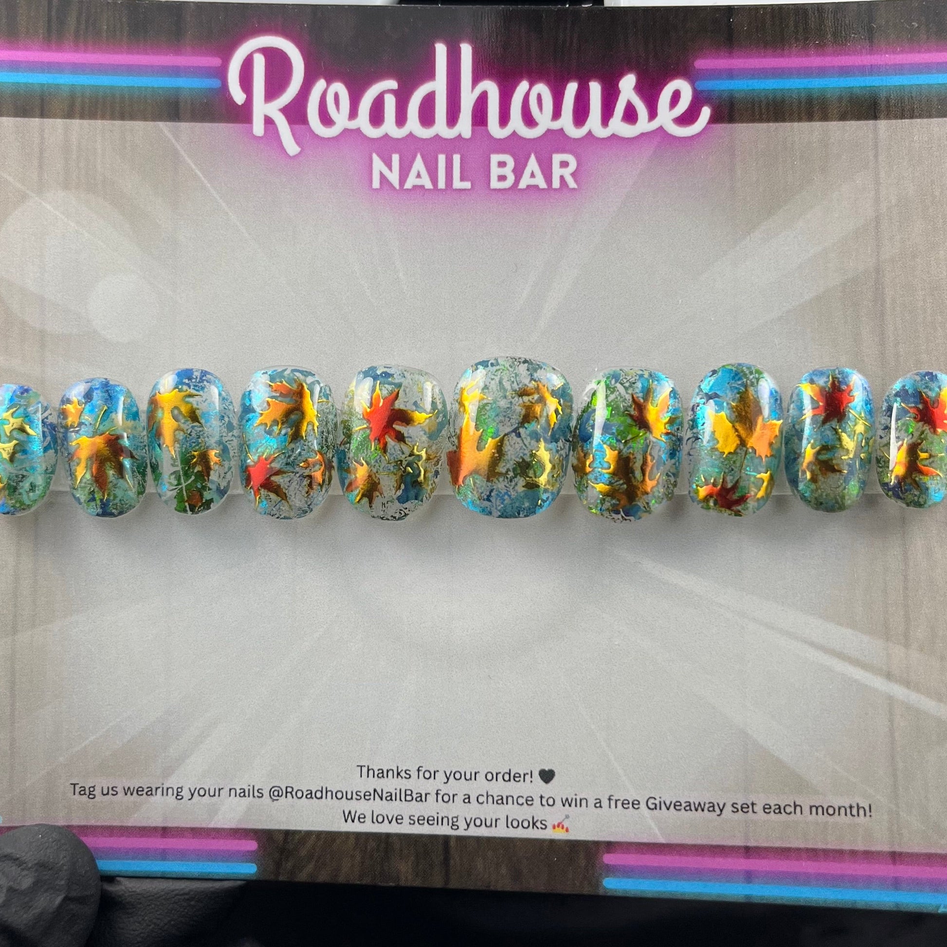 Hand-painted press-on nails with glass-effect base, aqua foiling, and metallic copper autumn leaves, displayed on Roadhouse Nail Bar backing card.