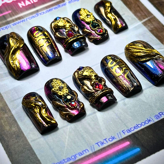 Hand-painted press-on nail set with black-purple multichrome base, featuring 3D gold Hamsa hand, snakes, and gothic baroque embellishments.

