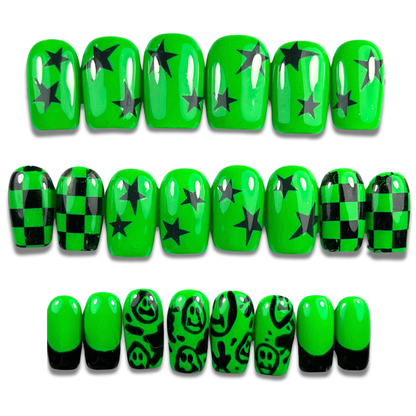 Hand with neon green and black press-on nails in short square shape featuring smiley faces, checkerboard, and punk-inspired designs – 24-piece set
